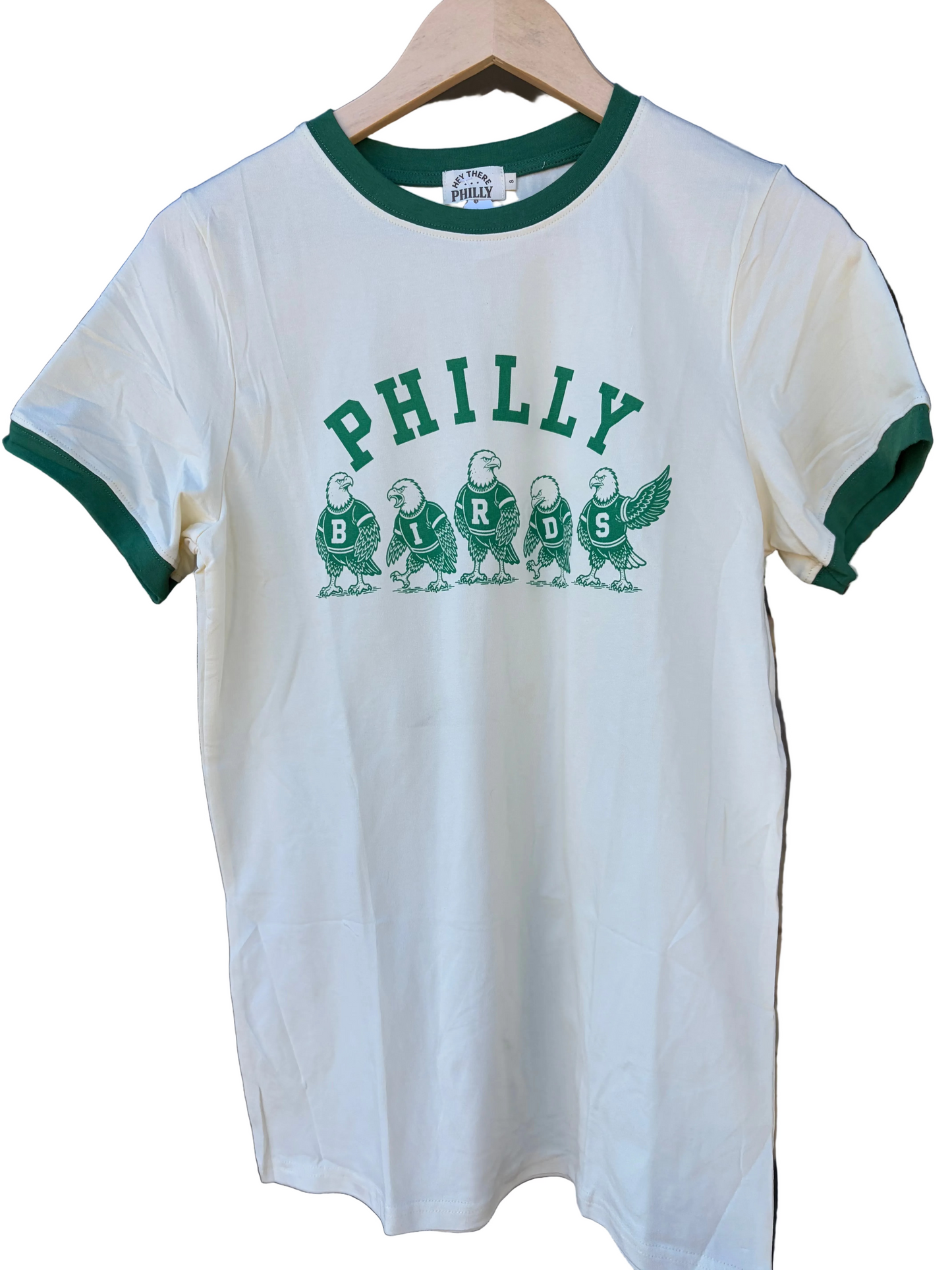 A white ringer t-shirt with green trim on the collar and cuffs, featuring a green graphic of five birds under the text 'PHILLY BIRDS' on the front, hanging on a wooden hanger.